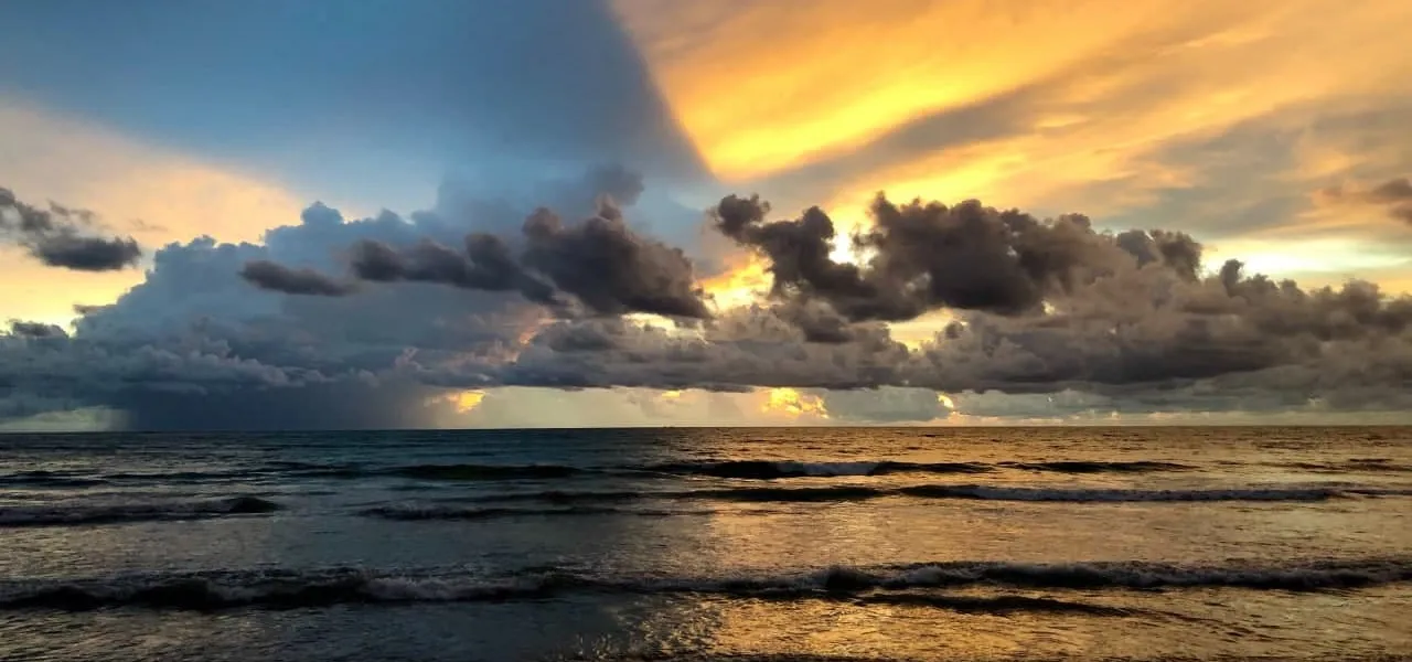 Golden light and dramatic clouds over the sea above a quiet sandy beach on Thailand’s Gulf coast